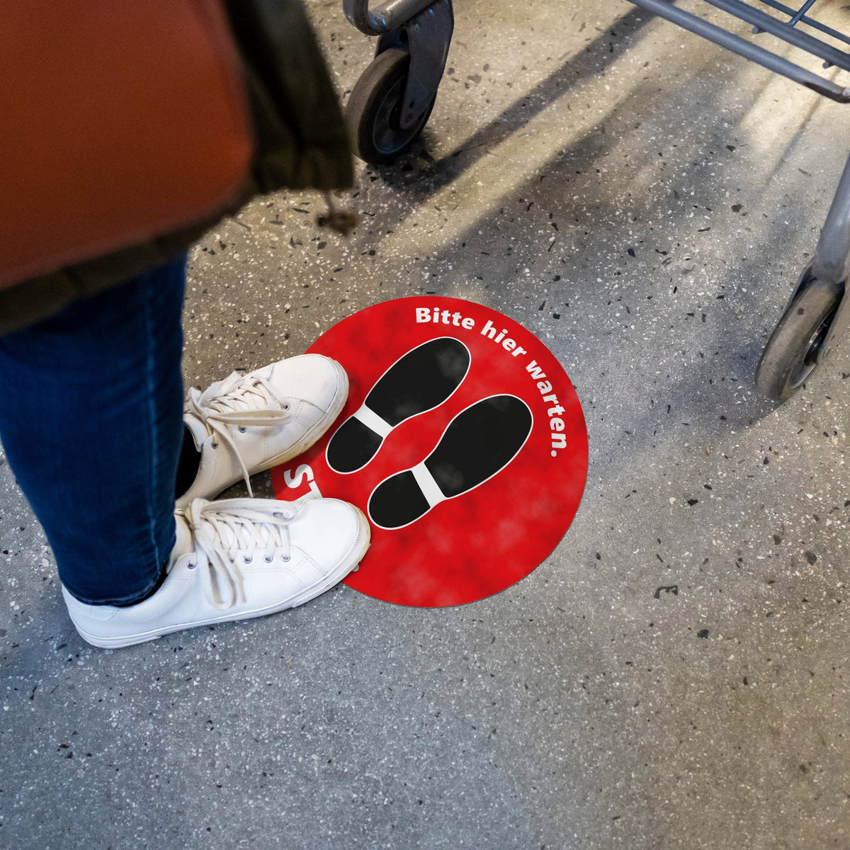 Bodenaufkleber STOP! Bitte hier warten rot vor einer Kasse, Kunde steht auf dem Wartepunkt